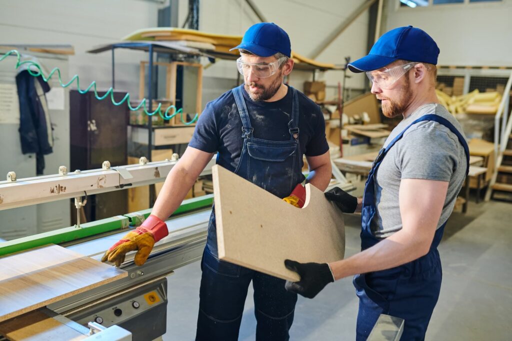 Anstoßkappe im Arbeitsschutz – Beschäftigte mit Kopfschutz und Schutzbrillen bei Arbeiten in einer Holzwerkstatt