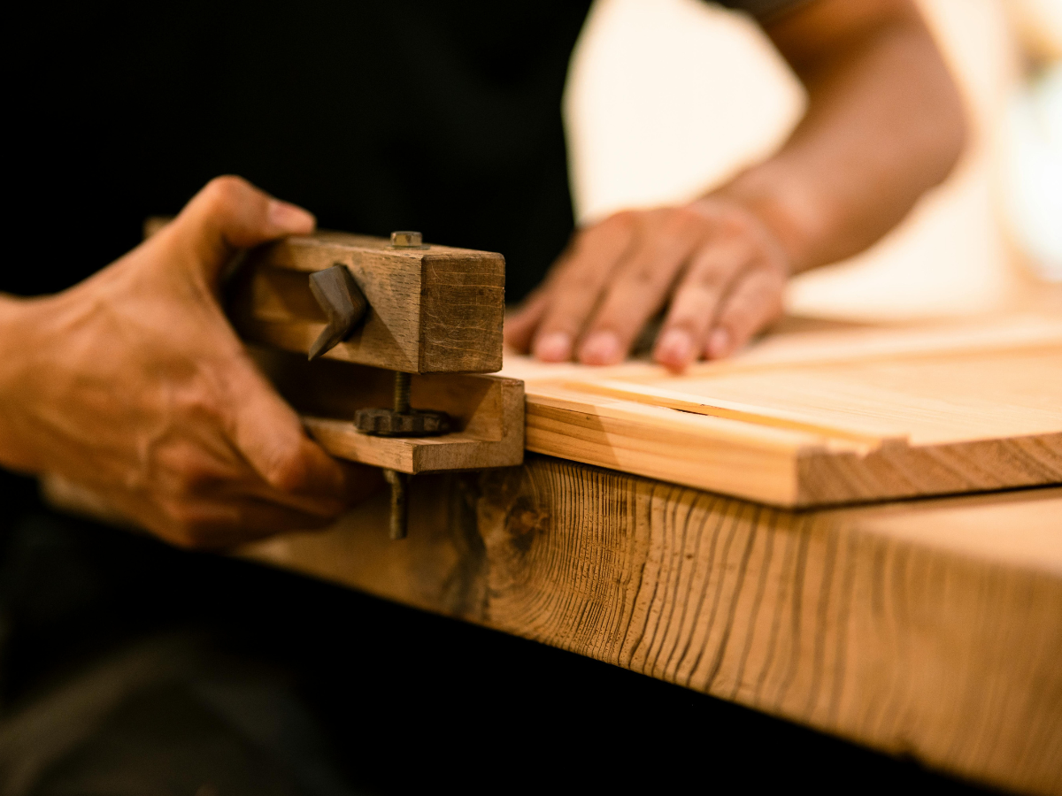 Handwerker bearbeitet ein Holzbrett mit einem Handhobel in einer Tischlerei